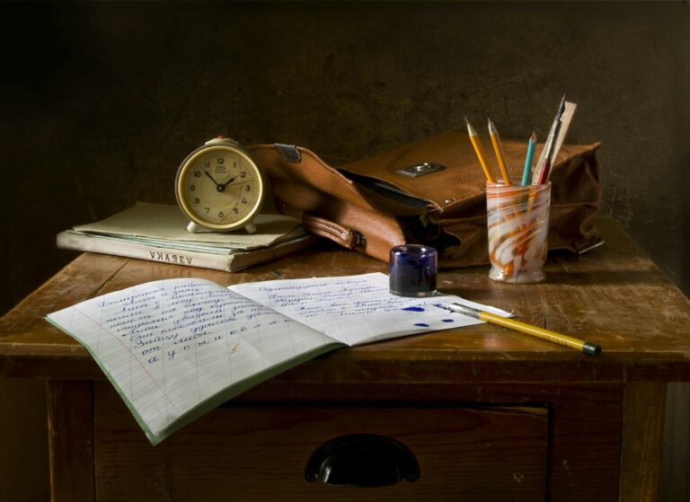 Classic wooden desk with writing materials, vintage clock, and a leather bag.